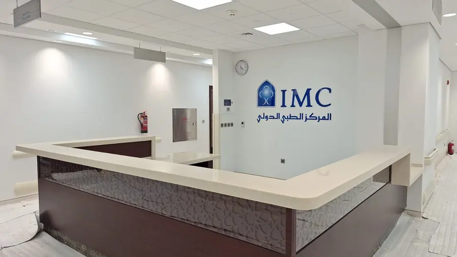 محطة تمريض قريبة من الإنجاز بسطح كريمي منحنٍ من السطح الصلب وشعار المركز الطبي الدولي (IMC) على الجدار خلفها