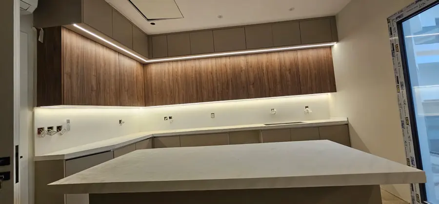Kitchen with walnut-finish wall cabinets, strip lighting and a white solid-surface island