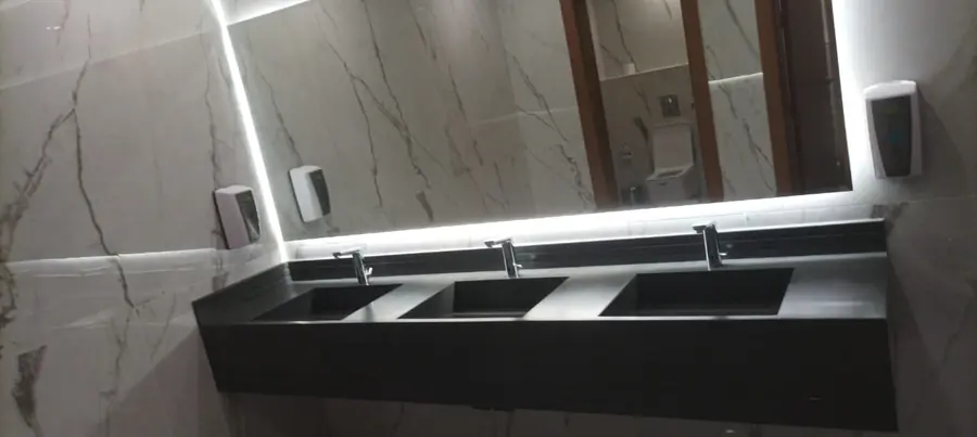 Dark solid-surface vanity with three integrated basins under a backlit mirror
